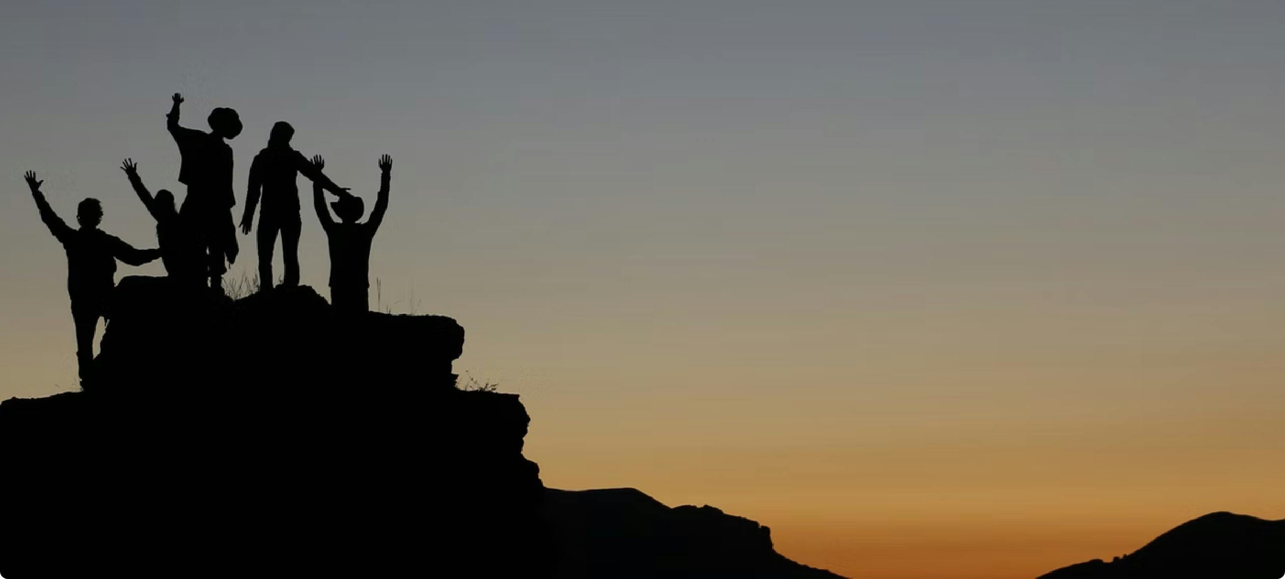 People from the top of a rock raising their arms under a sunset.